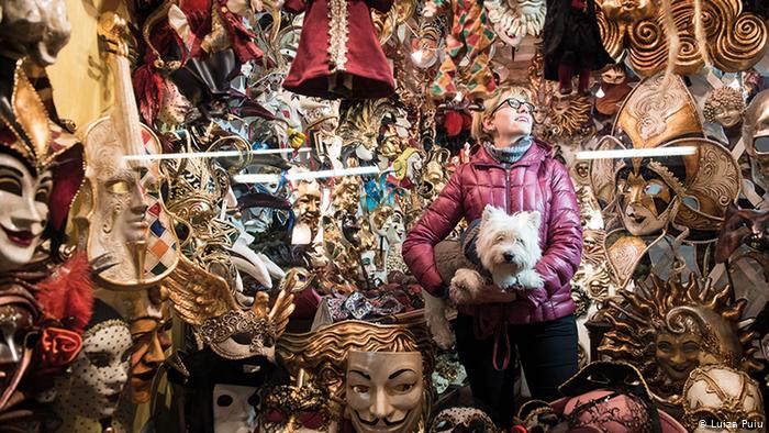 Женщина с собакой на руках на фоне итальянских масок